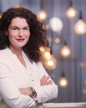 Portrait d'une femme en veste blanche devant une suspension d'ampoules